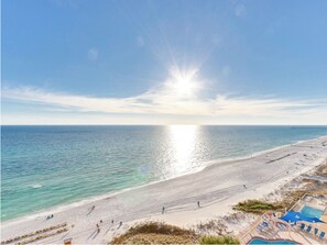 A beach with a clear sky, a sun reflecting on the water, and a pool area with lounge chairs. - Sunrise 2401 - Penthouse Gulf Front Paradise, Beach Service Included (Panama City Beach)
