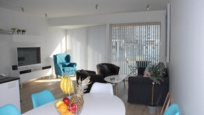 A modern living room with a white dining table, blue chairs, a black sofa, and a TV. - Scandinavian Apartments (Reykjavik)