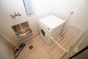 Un espace buanderie compact comprenant un lave-linge, un évier en métal et un étendoir.