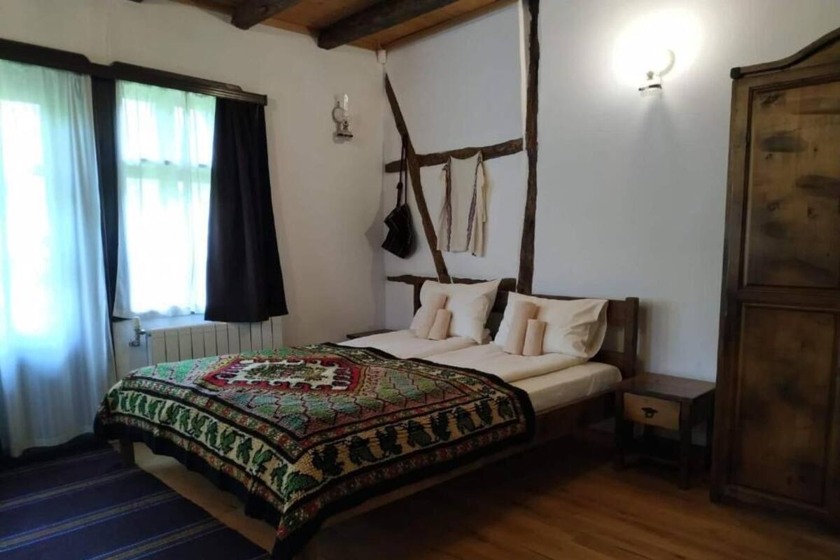 Un dormitorio con una cama de madera, una colcha estampada, una mesita de noche, un armario y una ventana con cortinas.
