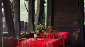 Een rustieke houten eetruimte met een tafel gedekt voor vier personen, omringd door houten stoelen.