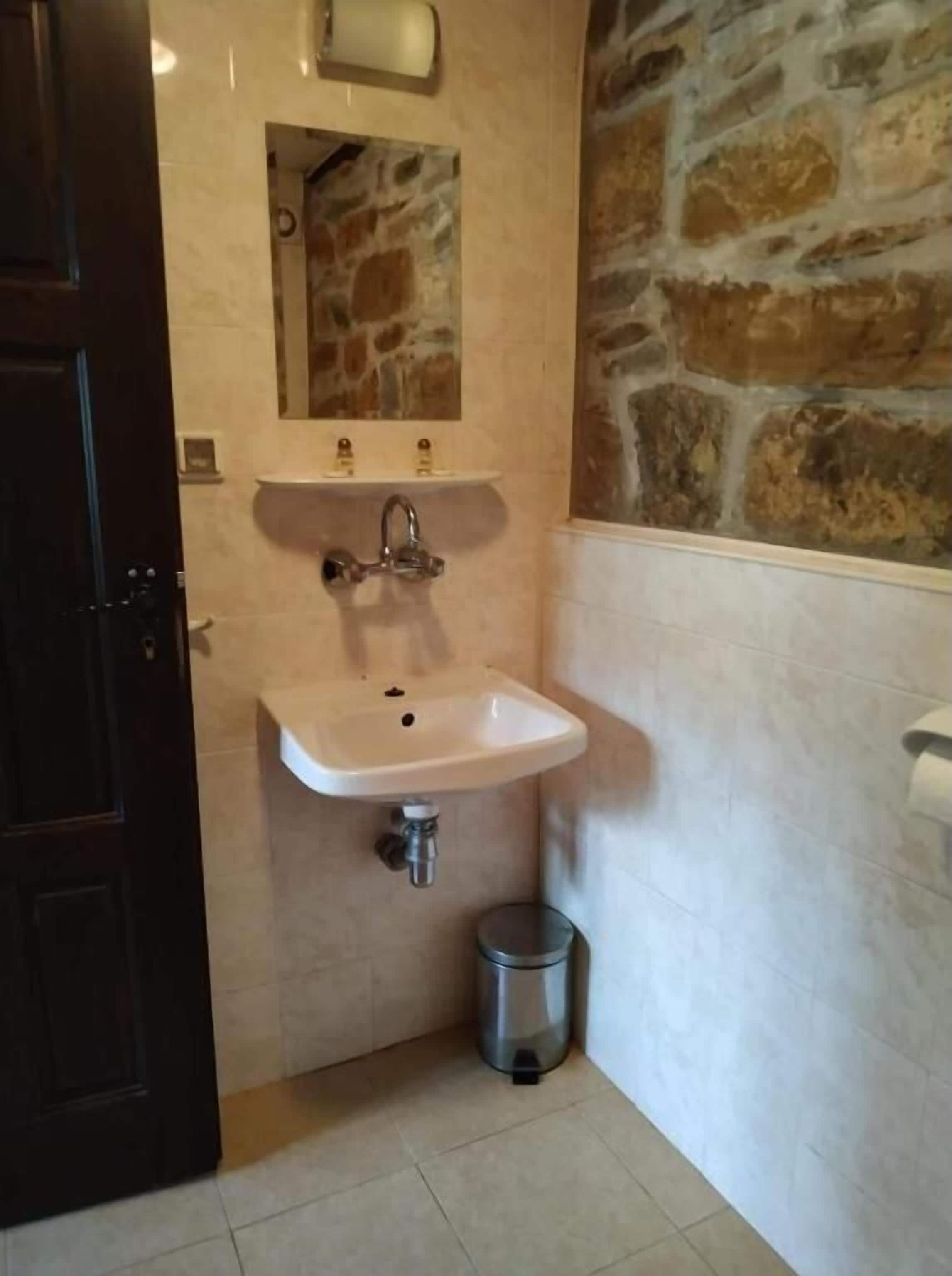 A bathroom with a white sink, a mirror, and a stone wall.