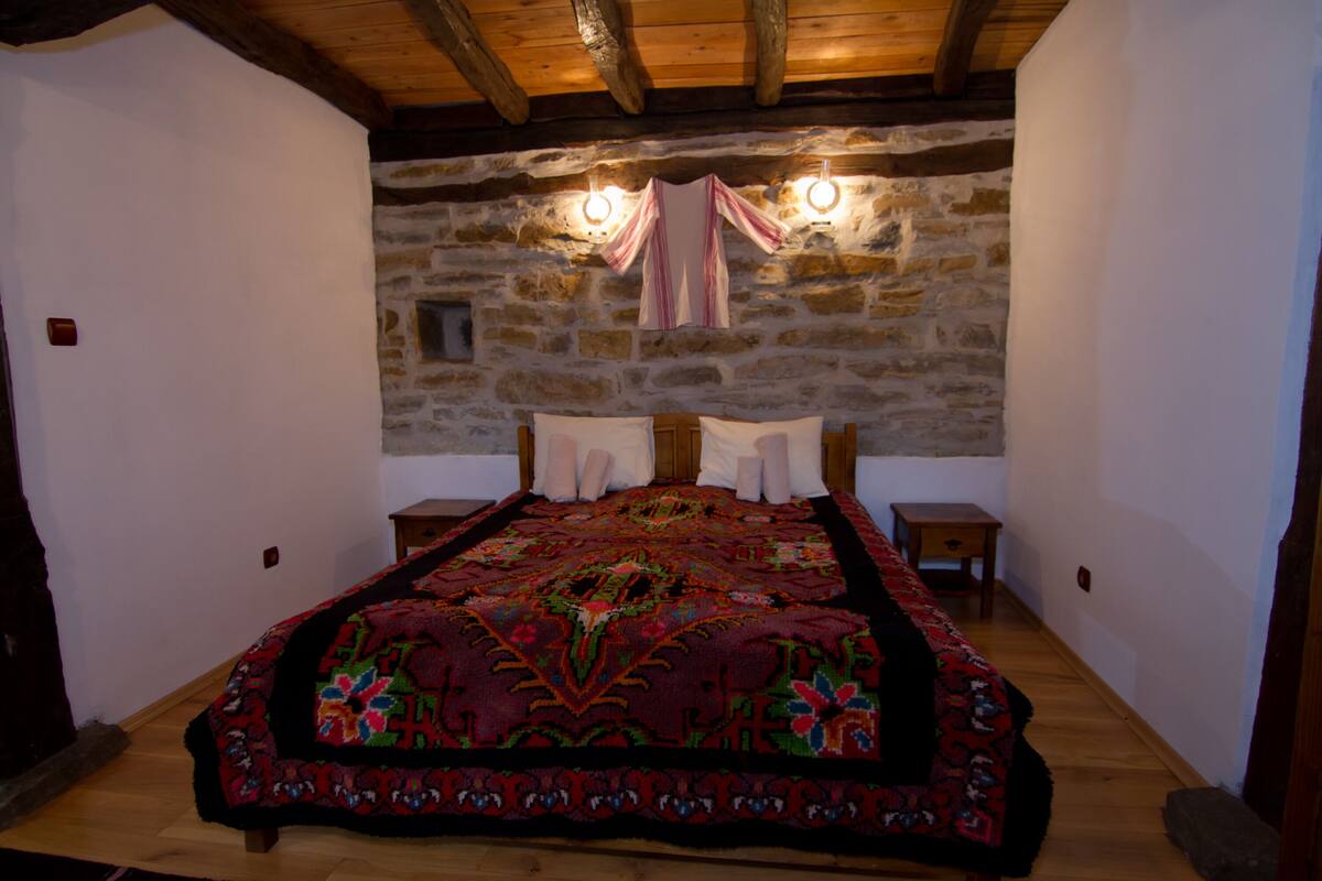 Un dormitorio con una cama grande, paredes de piedra, vigas de madera y dos lámparas de noche.