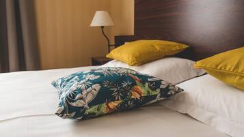 Una cama impecable con sábanas blancas y dos almohadas, una con estampado tropical y la otra amarilla.
