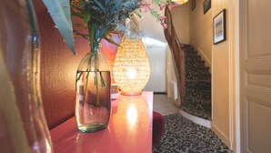 A hallway with a staircase, a vase with flowers, and a lit lamp.