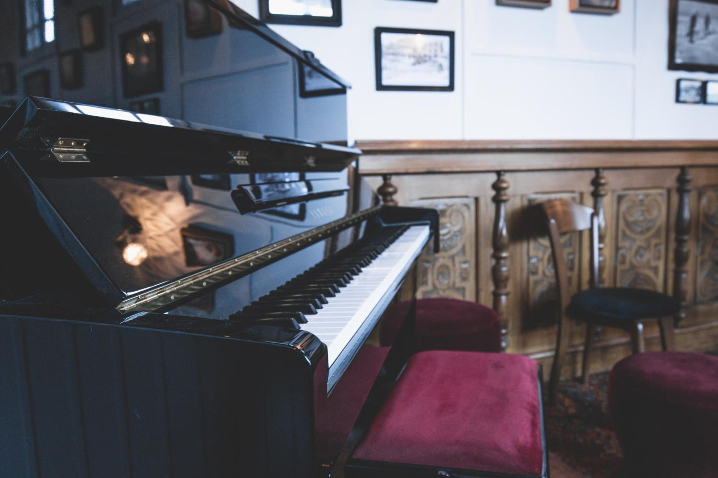 A grand piano in a room with ornate wood paneling and a red cushioned bench.