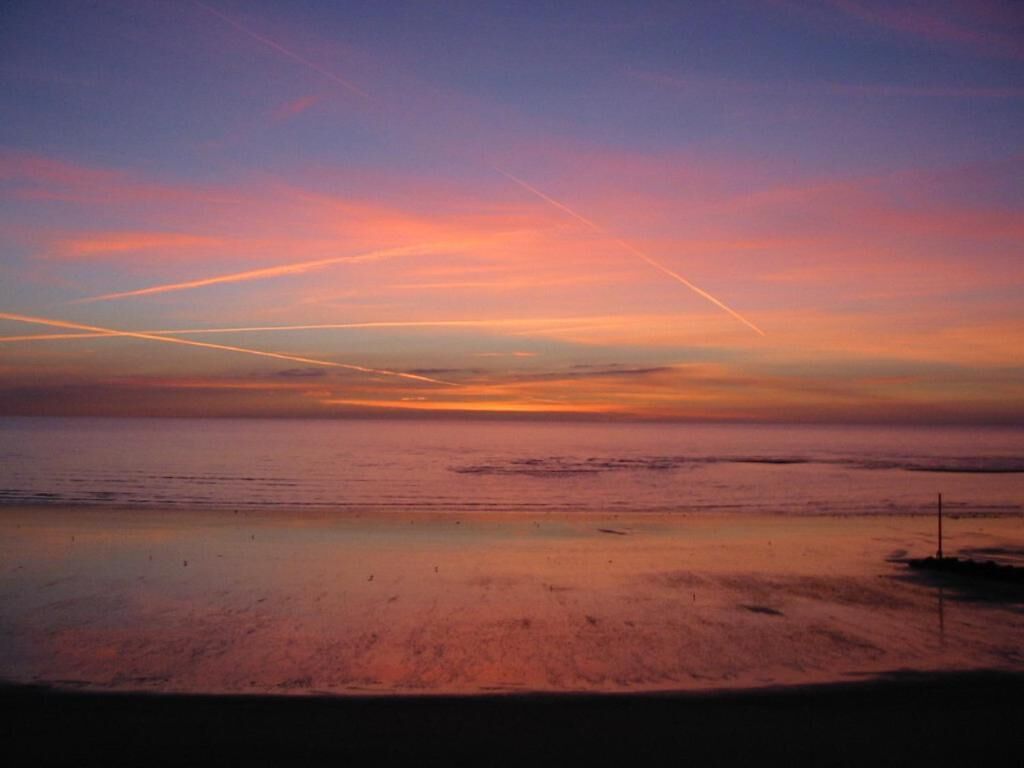 A beach with a sunset and contrails in the sky.