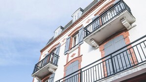 A multi-story building with balconies, red brick and white facade, and a clear sky.
