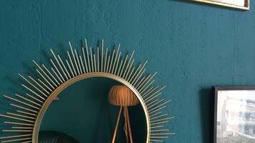 Una pared azul aguamarina con impresiones botánicas enmarcadas, un espejo con diseño de sol y una lámpara colgante.