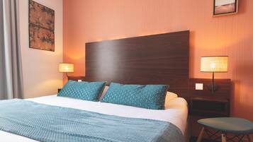 Een hotelkamer met een groot bed, twee wandlampen, een klein krukje en een lijst met een afbeelding aan de muur.