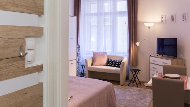 Un dormitorio con cama, escritorio y silla, televisor y ventana con cortinas.