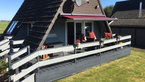 Een huis met een schuin dak, een schotelantenne en een overdekte veranda met rode stoelen.