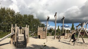 Een speeltuin met verschillende houten speeltoestellen en een glijbaan.