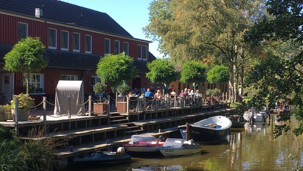 Een gracht met aanmerende boten, een voetgangersbrug en een gebouw met ramen in het rood.
