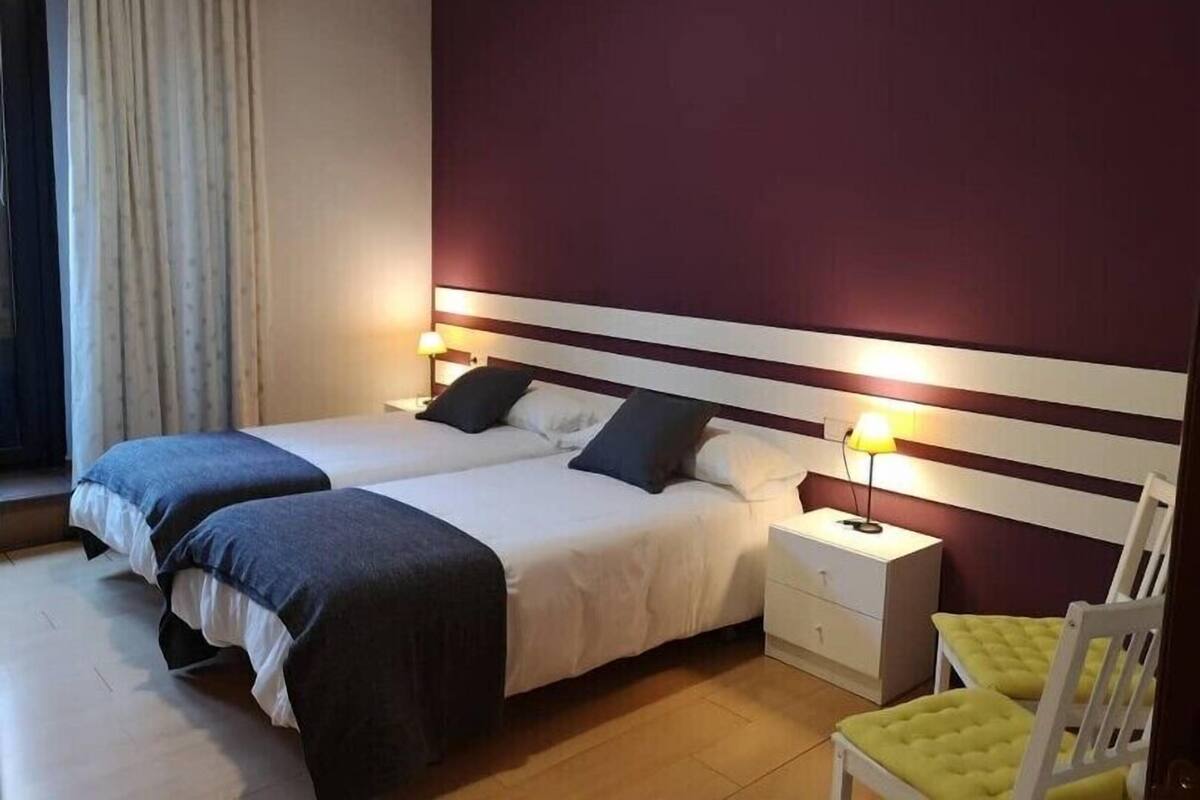 A double bed with two pillows, a nightstand with a lamp, and a yellow chair.