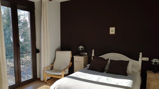 A bedroom with a bed, chair, nightstands, and a view through a door. - Hostal San Martín (León)
