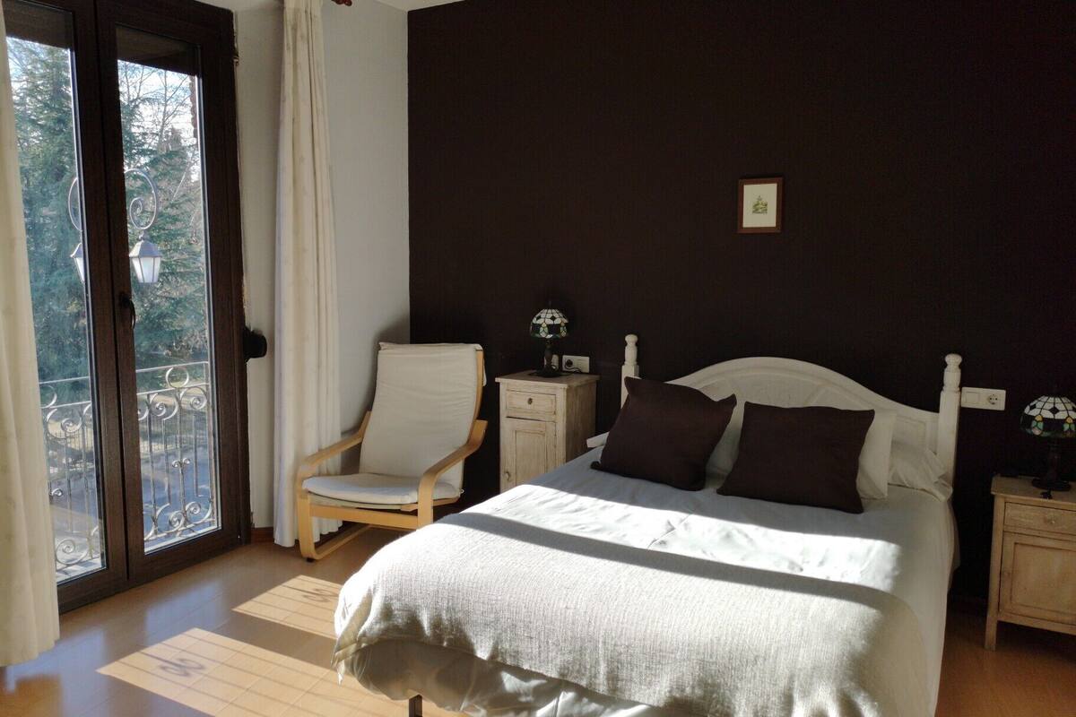 A bedroom with a bed, chair, nightstands, and a view through a door.