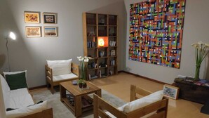A cozy living room with a bookshelf, a colorful abstract painting, and a vase of flowers. - Hostal San Martín (León)