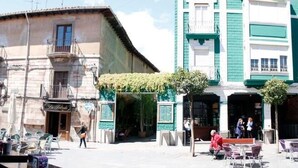 A courtyard with outdoor seating, a building with a balcony, and a green awning. - Hostal San Martín (León)