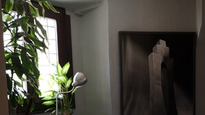 A room with a large window, a potted plant, a floor lamp, and a framed artwork on the wall. - Hostal San Martín (León)