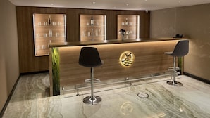 A modern reception area with a wooden reception desk, three bar stools, and shelves displaying glassware and bottles. - Radar Otel (Istanbul)