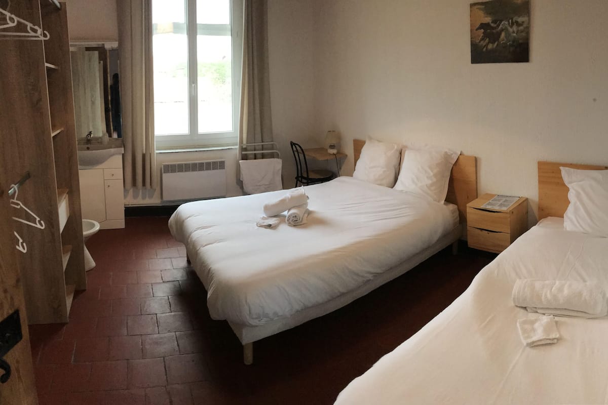 Een hotelkamer met twee bedden, een houten kledingkast, een badkamer met wastafel en toilet, en een raam met gordijnen.