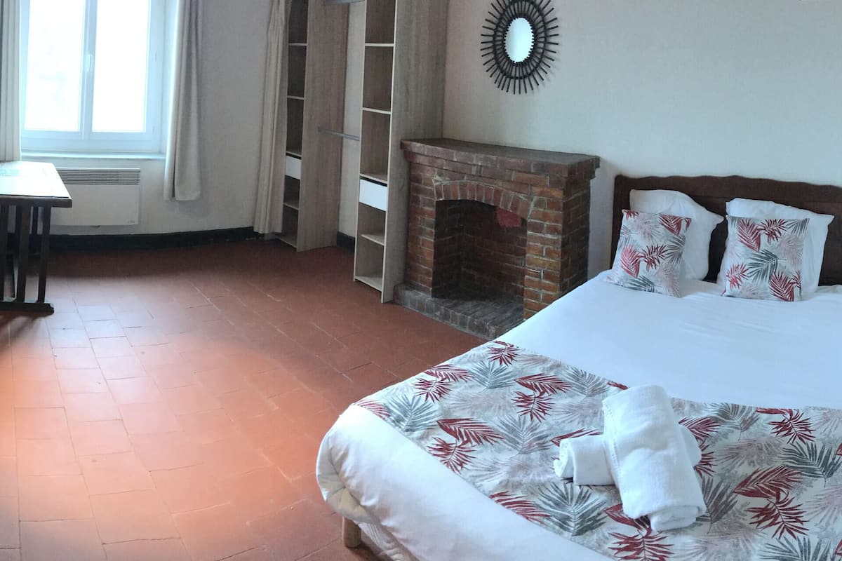 Een hotelkamer met twee bedden, een klein tafeltje, een open haard en een raam met gordijnen.