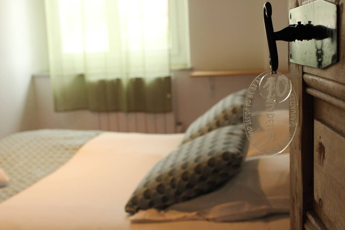 Een slaapkamer met een bed, kussens en een houten dressoir met spiegel.