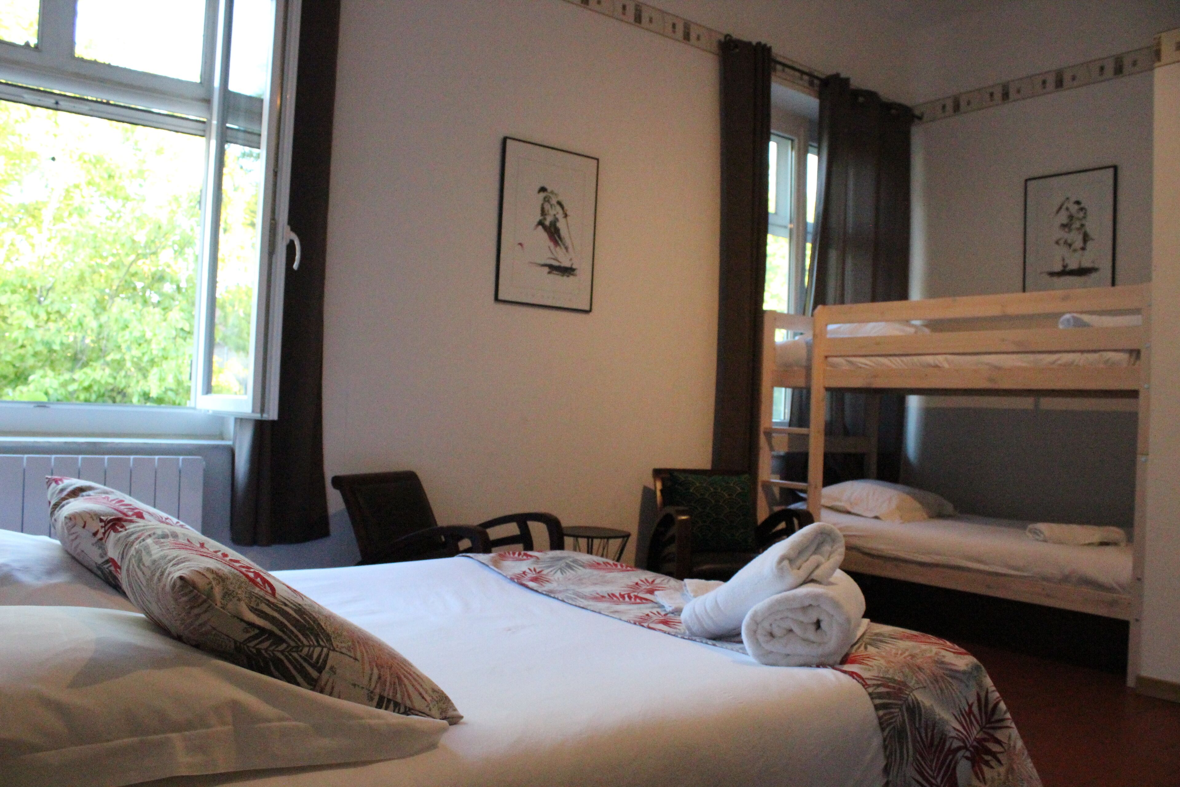Ein Hotelzimmer mit einem Bett, einem Schlafplatz, einem Fenster mit Vorhängen und gerahmten Bildern an der Wand.