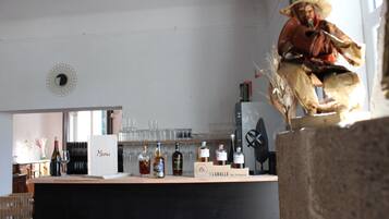Un espace bar au décor rustique, comprenant un comptoir en bois et une statue. On peut y voir diverses bouteilles et différents types de verres sur le comptoir, ainsi qu’un panneau indiquant le menu.