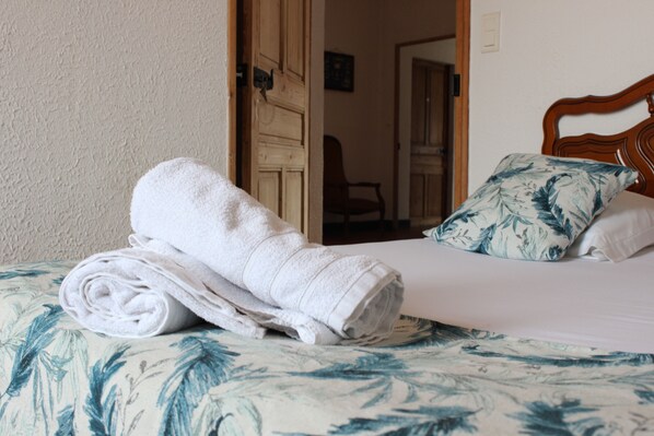 A neatly made bed with a floral bedspread and a rolled white towel on it. - Hôtel Restaurant Les Saladelles (Arles)
