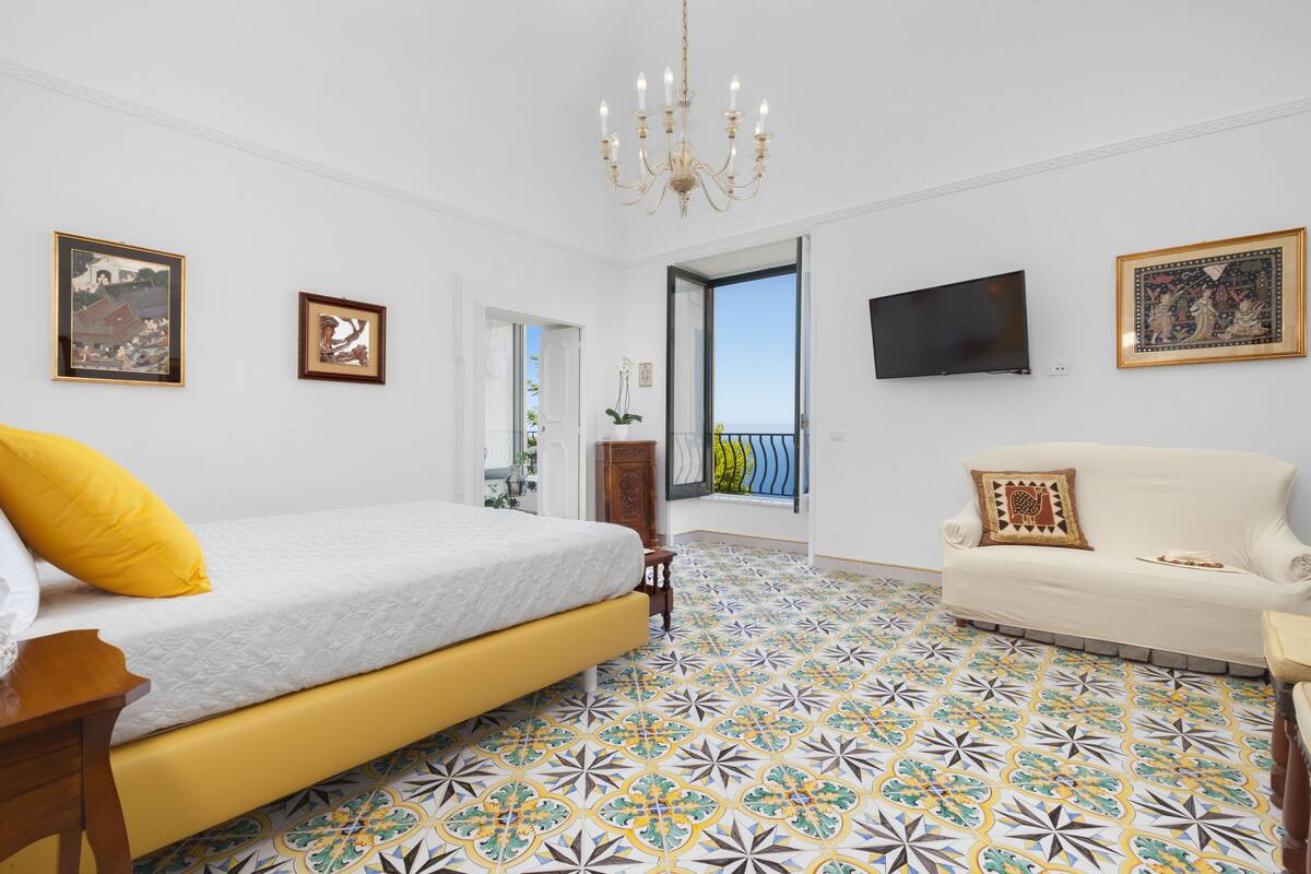 A bedroom with a bed, a sofa, a TV, and a balcony.