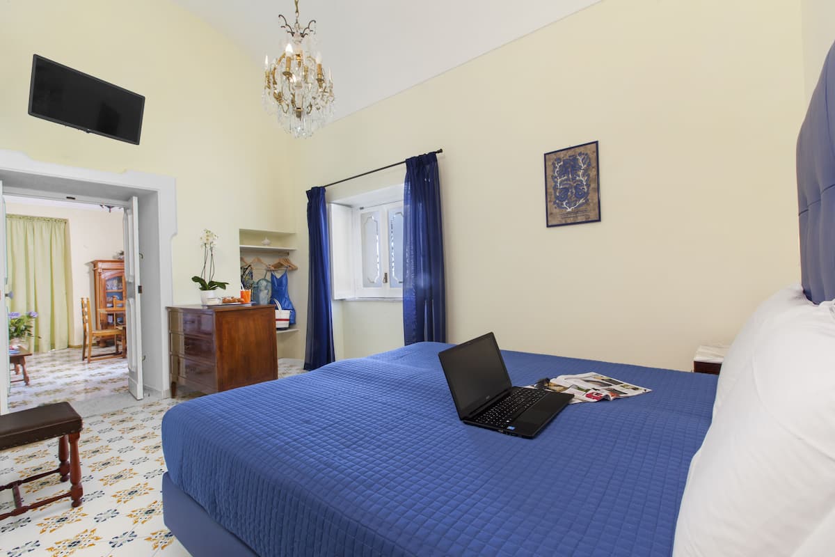 A bedroom with a bed, a laptop, a chandelier, a television, and a painting.