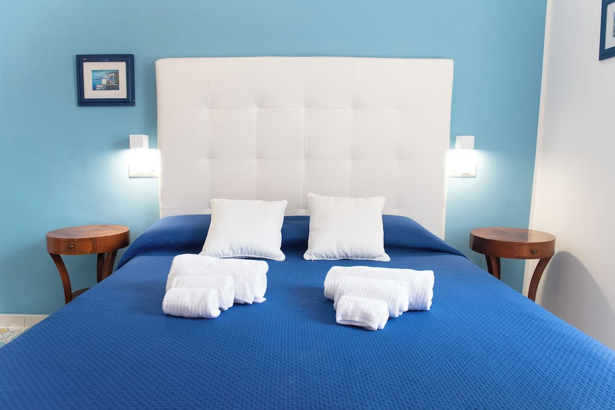 A neatly made bed with blue bedding and white pillows, two bedside tables with lamps, and a framed picture on the wall.