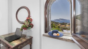 A laptop on a wooden table, a vase with flowers, and a view of a coastal landscape through an arched window. - Torre Elisabetta (Massa Lubrense)