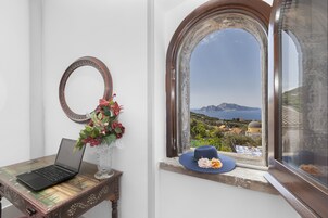 A laptop on a wooden table, a vase with flowers, and a view of a coastal landscape through an arched window.