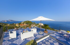 Terraço no topo do edifício com chão azul estampado, mobiliário de exterior branco e um grande guarda-sol branco.