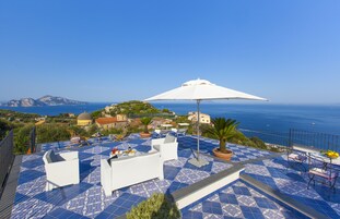 A rooftop terrace with blue patterned flooring, white outdoor furniture, and a large white umbrella.