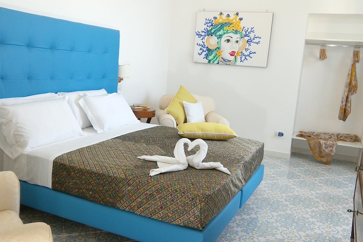 A bed with white and blue bedding, a patterned bedspread, and a heart-shaped towel on the bed.