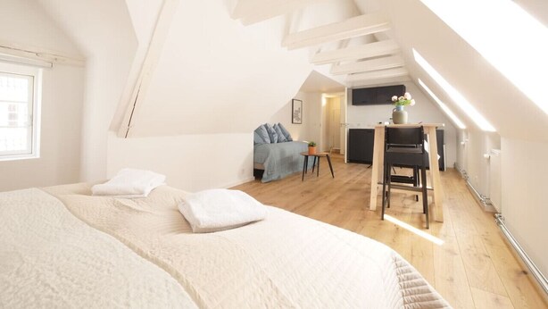 A bedroom with a large bed, a desk, and a chair. There is a window and a door in the room. - Rent A Place 4, Copenhagen (København)