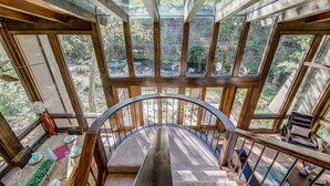 Ein großzügiger Innenraum mit einer geschwungenen Treppe, die zu einem Balkon führt, umgeben von großen Fenstern mit Blick auf eine bewaldete Landschaft.