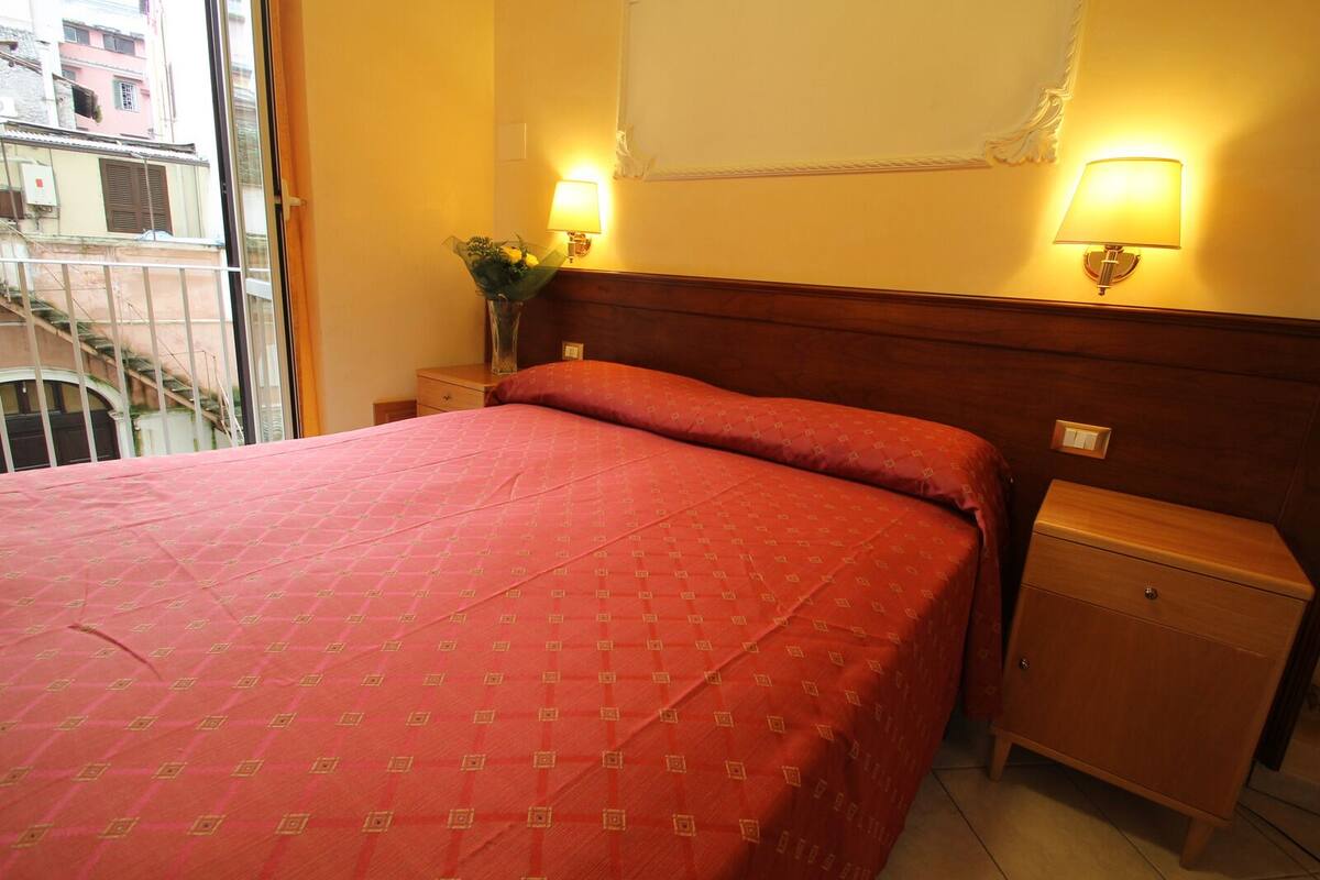 A hotel room with a large bed, two bedside tables, and two wall-mounted lamps.