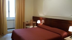 A hotel room with a bed, a desk, a chair, a lamp, and a window with curtains. - Hotel Rosetta (Rome)