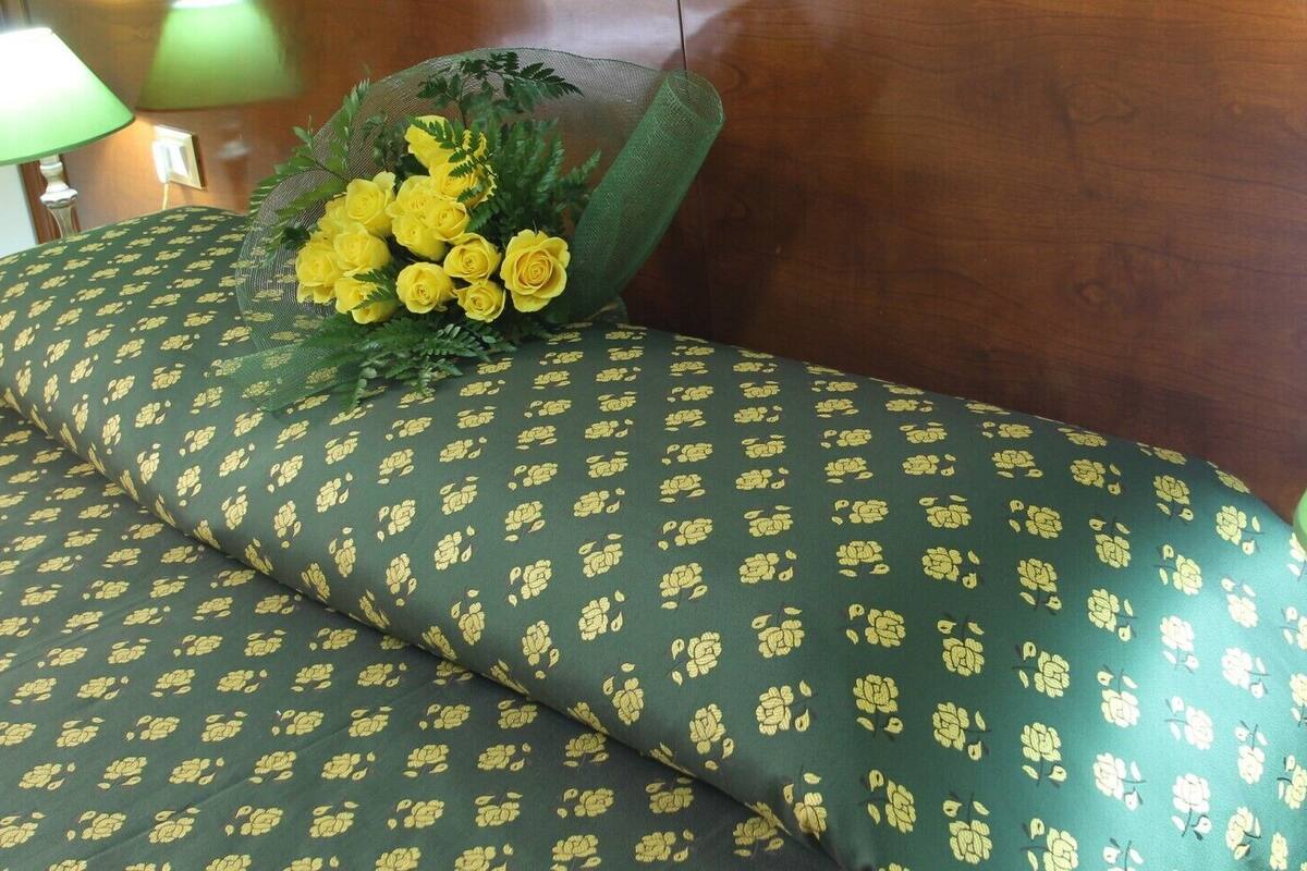 A hotel room with green patterned bedding, a decorative flower arrangement, and two bedside lamps.