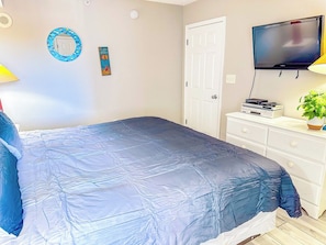 A bedroom with a bed, a television, a dresser, and a door.