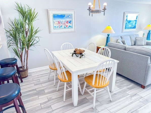 A dining area with a white table and chairs, a grey sofa, and a potted plant.