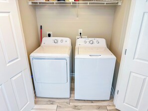 A laundry room with two front-loading washing machines and a shelf above them.