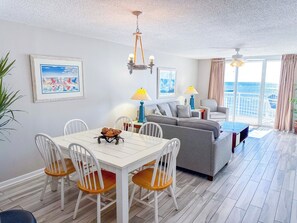 A modern living room with a dining area, a grey sofa, and a balcony with curtains. - South Shore Villas 803 (North Myrtle Beach)