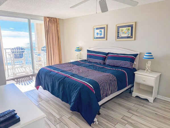 A bedroom with a large bed, a nightstand, a ceiling fan, and a view of the balcony.