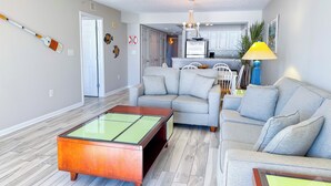 Una sala de estar moderna con un sofá gris, una mesa de centro de vidrio y una cocina al fondo.